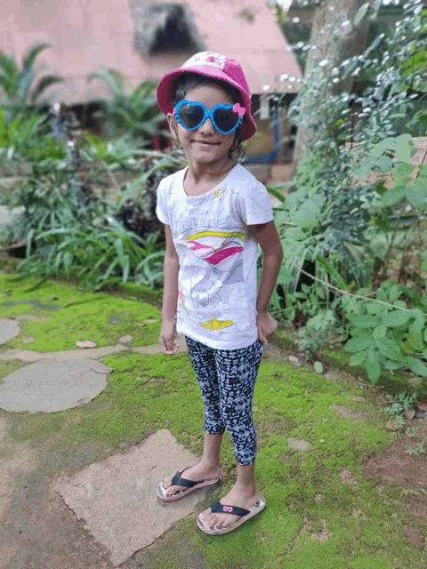 a little girl wearing sunglasses and a pink hat is standing in the grass