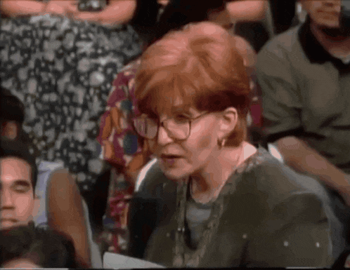 a woman with red hair and glasses sits in a crowd