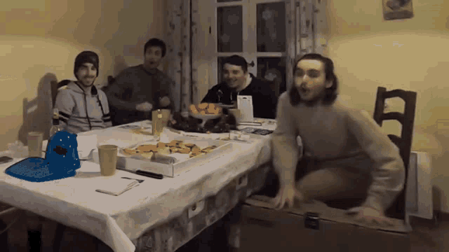 a group of men are sitting around a table with a box of pizza on it