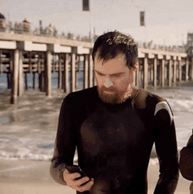 a man in a wet suit looks at his phone on the beach
