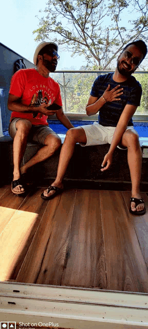 a man in a red los angeles shirt sits next to a man in a blue shirt