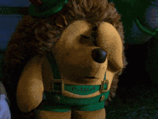 a stuffed hedgehog wearing green pants and a belt that says ' erick ' on it