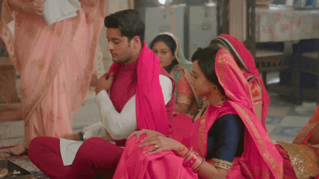 a bride and groom are sitting on the floor and the bride is holding the groom 's arm