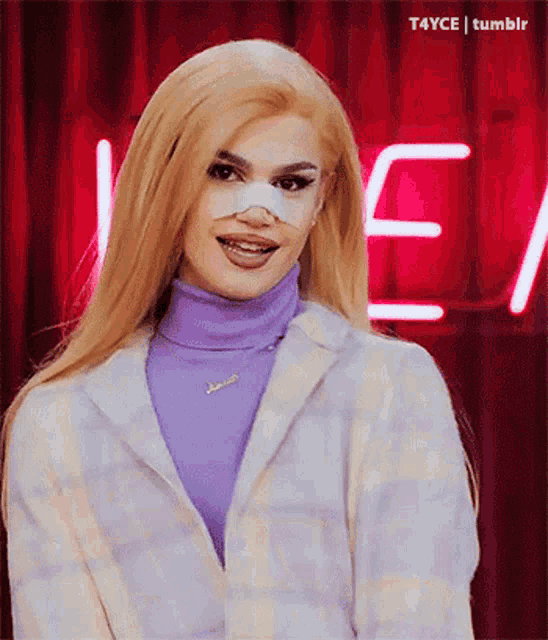 a woman wearing a purple turtleneck and a white jacket has a bandage on her nose