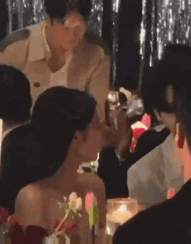 a group of people are sitting at a table and a woman is kissing a man on the cheek .