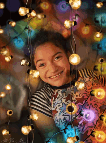 a young girl is smiling while surrounded by christmas lights and a picture of her was taken by fat vita m