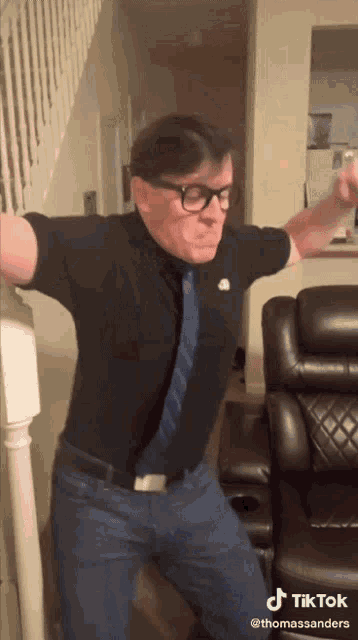 a man wearing glasses and a tie is dancing in front of a couch and stairs