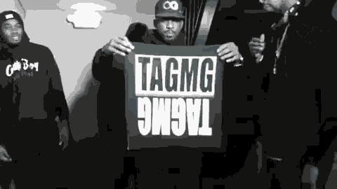 a black and white photo of a group of men holding a sign that says tagmg