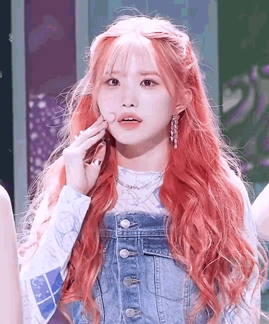 a girl with red hair and bangs is wearing a denim jumpsuit and a white shirt .