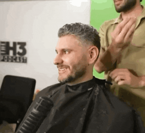 a man is getting his hair cut by a barber while wearing a cape .