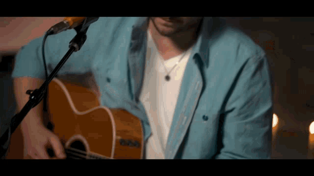 a man in a blue shirt is playing a guitar and singing into a microphone