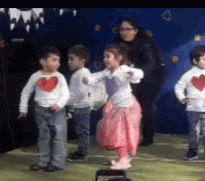 a group of young children are dancing on a stage while a woman watches .