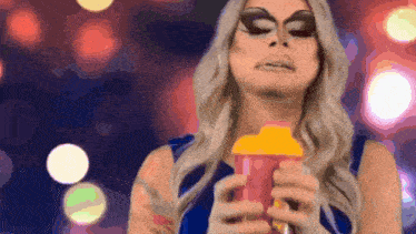 a drag queen is holding a pink and yellow cup