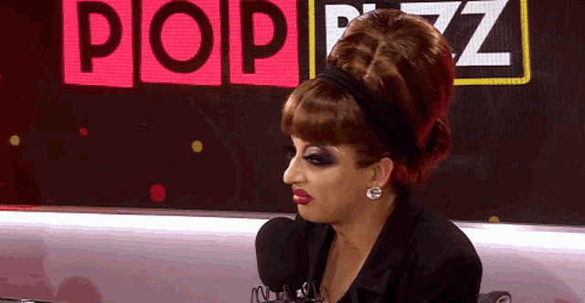 a woman in a wig is sitting in front of a sign that says pop
