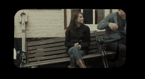 a woman sits on a wooden bench with a man sitting behind her