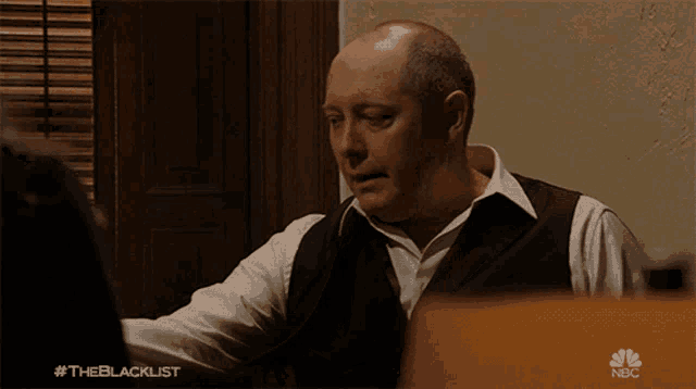 a man sitting in front of a laptop with the blacklist written on the bottom right