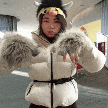 a woman wearing a furry hat and gloves holds her hands out
