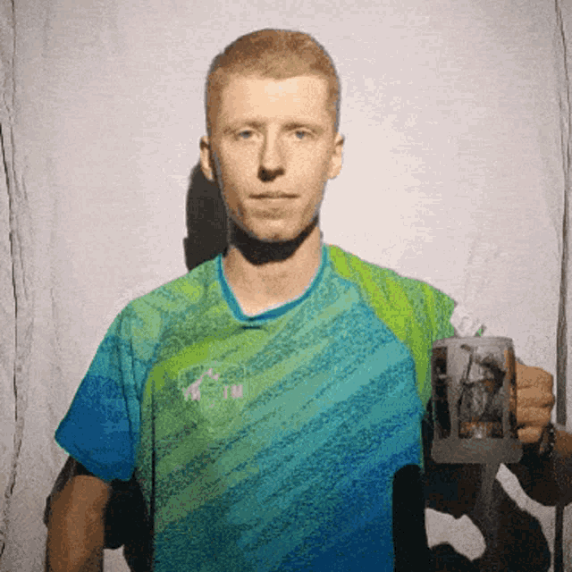 a man in a blue and green shirt is holding a cup