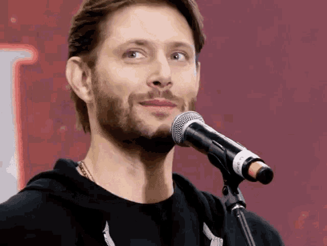 a man with a beard is singing into a microphone in front of a red background