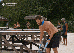 a man without a shirt is standing on a beach in front of a wooden fence that says neo enezioao