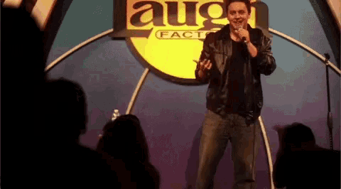 a man stands on a stage in front of a sign that says laugh factory