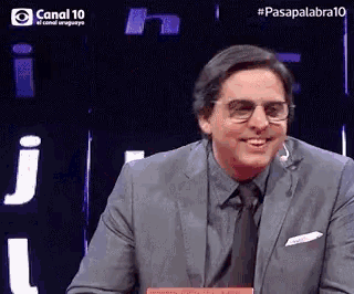 a man wearing glasses and a suit is smiling in front of a sign that says canal 10