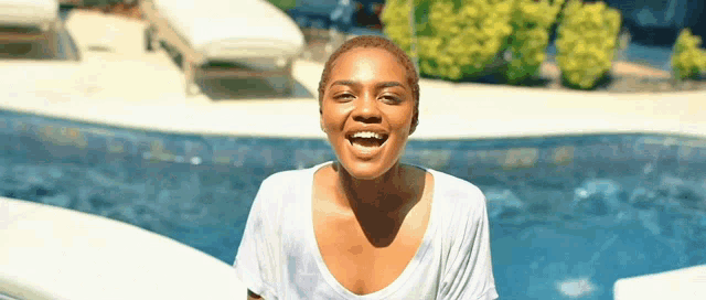 a woman in a white shirt is standing in front of a swimming pool and smiling .