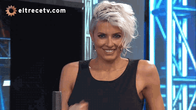 a woman in a black tank top is smiling in front of a screen that says eltrecetv.com