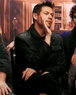 a man in a black jacket sits with his hand on his face