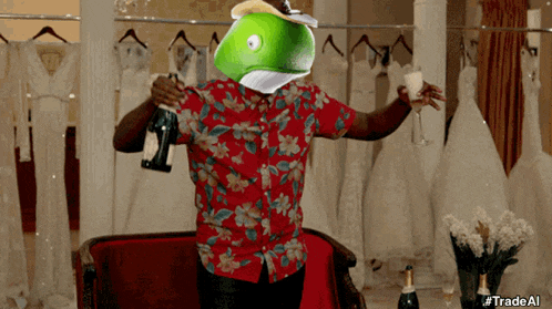 a man in a red shirt with a green fish on his head holds a bottle of champagne