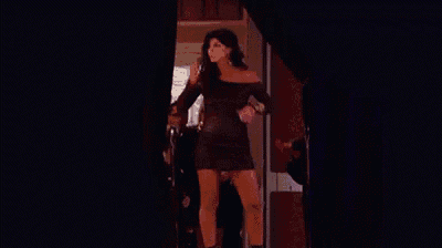 a woman in a black dress is standing in front of a black curtain in a room .