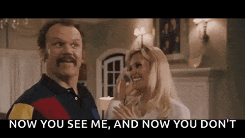 a man with a mustache is standing next to a woman in a living room and talking to her .