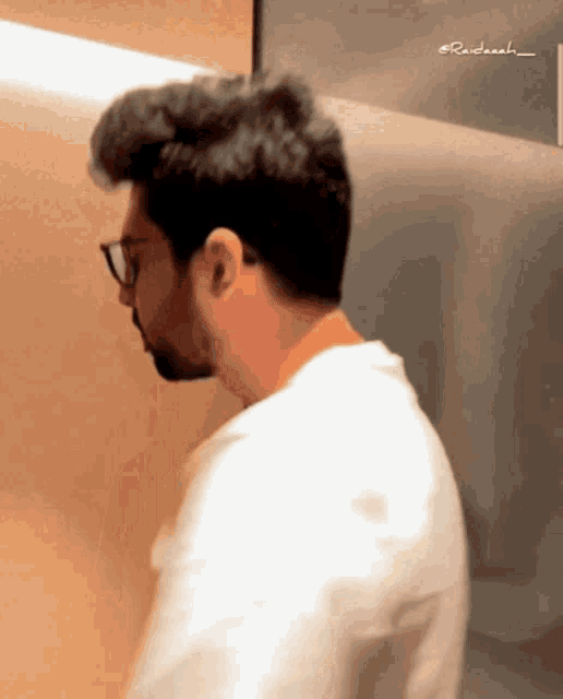 a man wearing glasses and a white shirt is standing in front of a wall that says ' raidaah ' on it