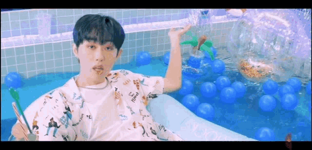 a young man is sitting in a swimming pool filled with blue balls .