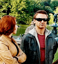 a man wearing sunglasses stands next to a woman in a park