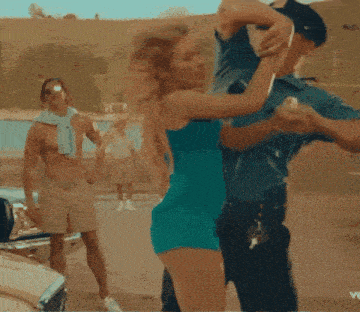 a woman in a blue dress is dancing with two police officers in front of a car