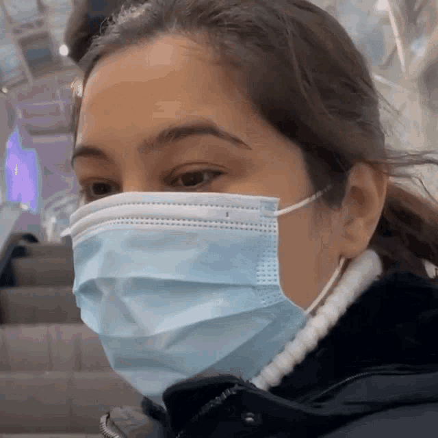 a woman wearing a blue face mask looks at the camera
