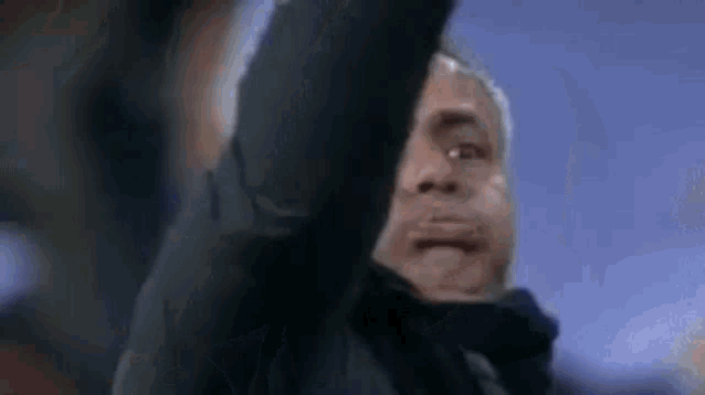 a man in a black jacket is raising his arm in the air in a close up .
