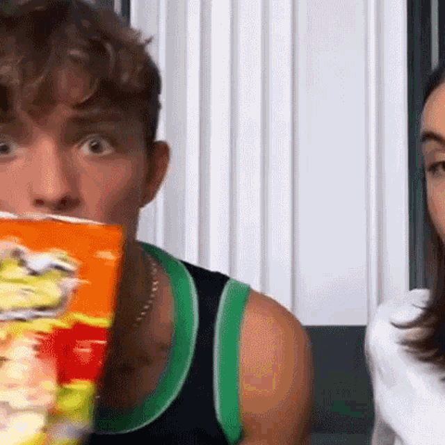 a man is holding a bag of chips in front of his face and a woman is looking at him .
