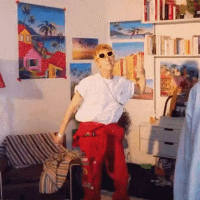 a man wearing sunglasses and red pants is dancing in a room