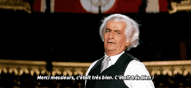 a man in a suit and tie stands in front of a crowd and says merci messieurs