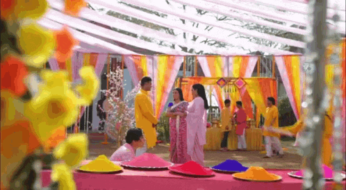 a group of people are standing around a table with plates of colored powder on it .