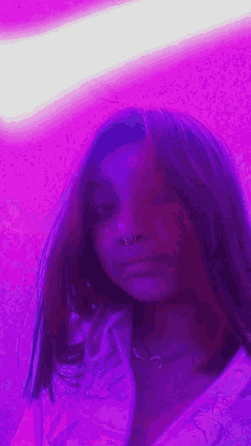 a close up of a woman 's face with a purple background and a nose ring .
