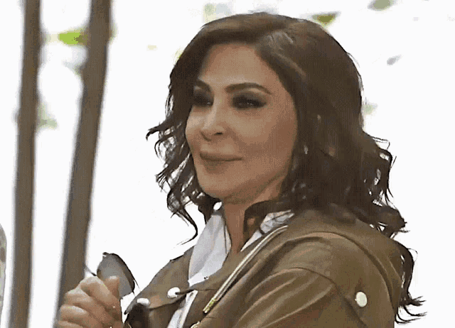 a woman in a green jacket is smiling and holding a cell phone