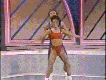 a man is carrying a woman on his shoulders while they are doing exercises on a stage .
