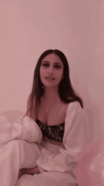 a woman in a black lace bra and white pants is sitting in front of pink balloons