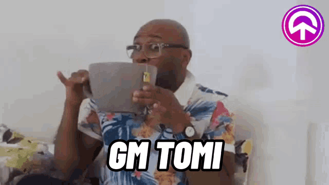 a man wearing glasses is sitting on a couch holding a tablet and saying `` gm tomi '' .