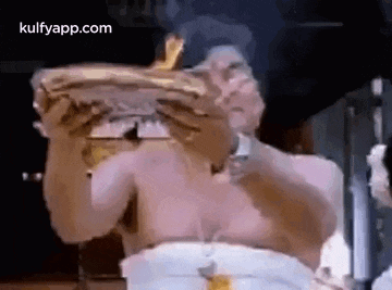 a shirtless man is sitting at a table eating a large hamburger .