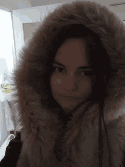 a woman wearing a furry hooded coat looks at the camera