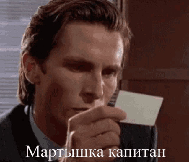 a man in a suit and tie is holding a card in his hand with the words " мартышка капитан " on it
